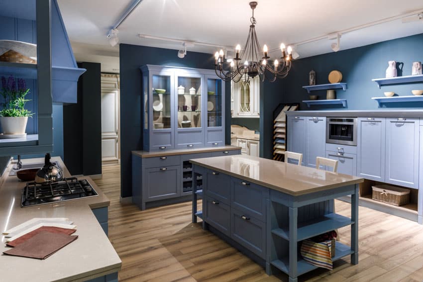 Blue country kitchen with freestanding cabinet, island, countertop, floating shelves, stove, wood floors, and chandelier