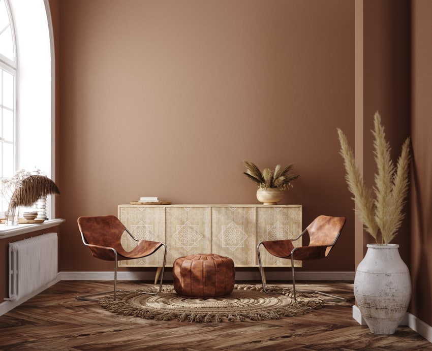 Brown rustic living room with dresser, chairs, pouf, floor vase, wooden flooring, heater, and window