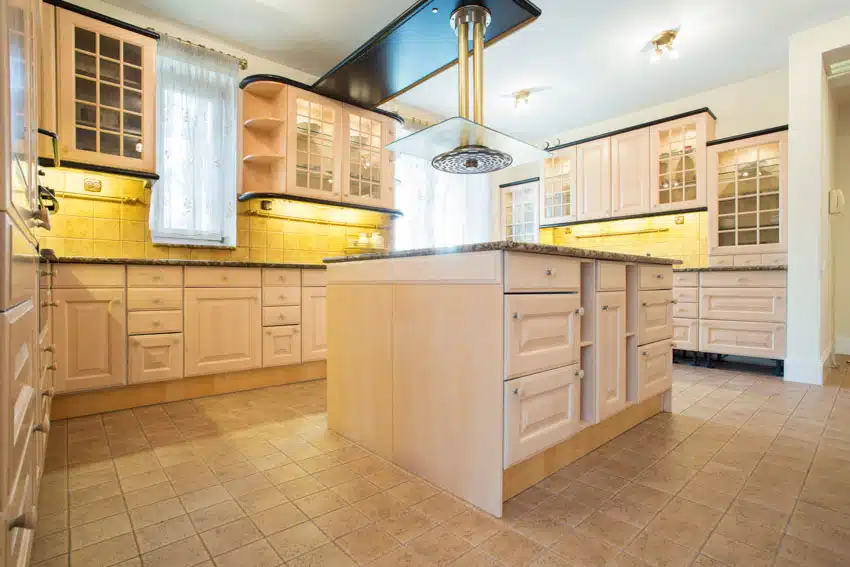 Classic kitchen with glass cabinets, countertop, travertine tile floor, range hood, and windows