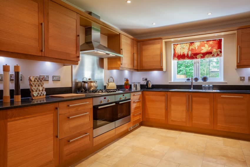 Classic kitchen with range hood, travertine floor, wood cabinets, window, countertop, sink, and faucet