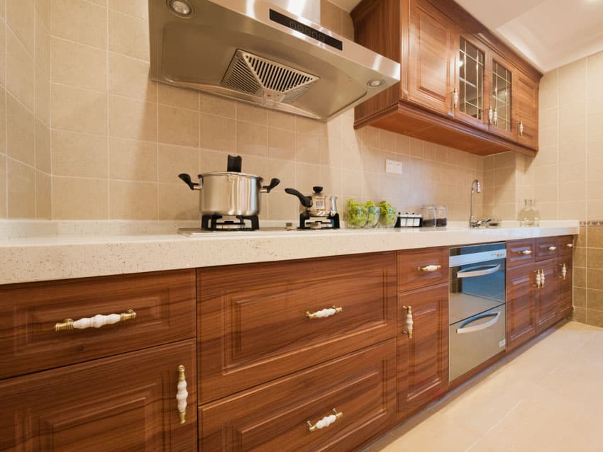 Classic kitchen with square tile backsplash, countertop, wood cabinets, drawers, stove, and range hood