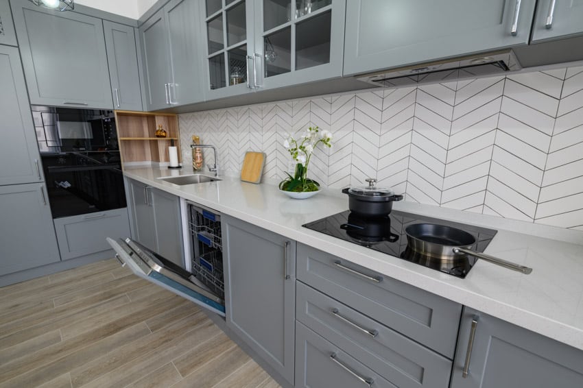 Contemporary kitchen with chevron matte backsplash tile, countertop, stove, wood floors, and cabinets