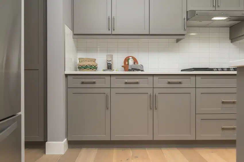 Kitchen with gray under sink cabinets, white subway tile backspash and pine wood flooring