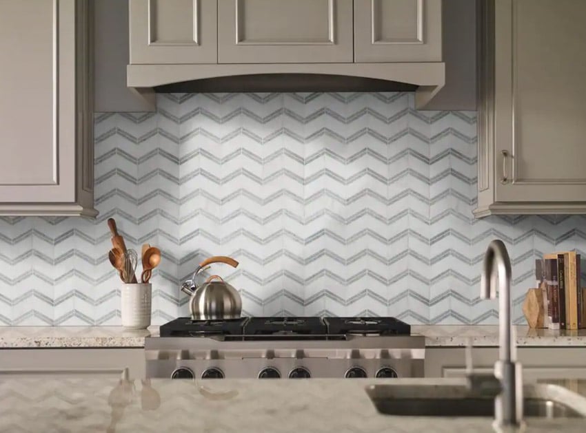 Contemporary kitchen with marble chevron tile backsplash, cream cabinets, stove, sink, faucet, and countertop