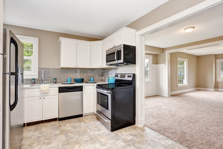 Contemporary kitchen with travertine tile floor, oven, stove, dishwasher, window, and white cabinets