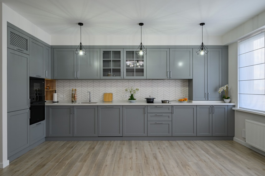 Contemporary kitchen with white chevron tile backsplash, wood flooring, gray cabinets, pendant lights, and windows