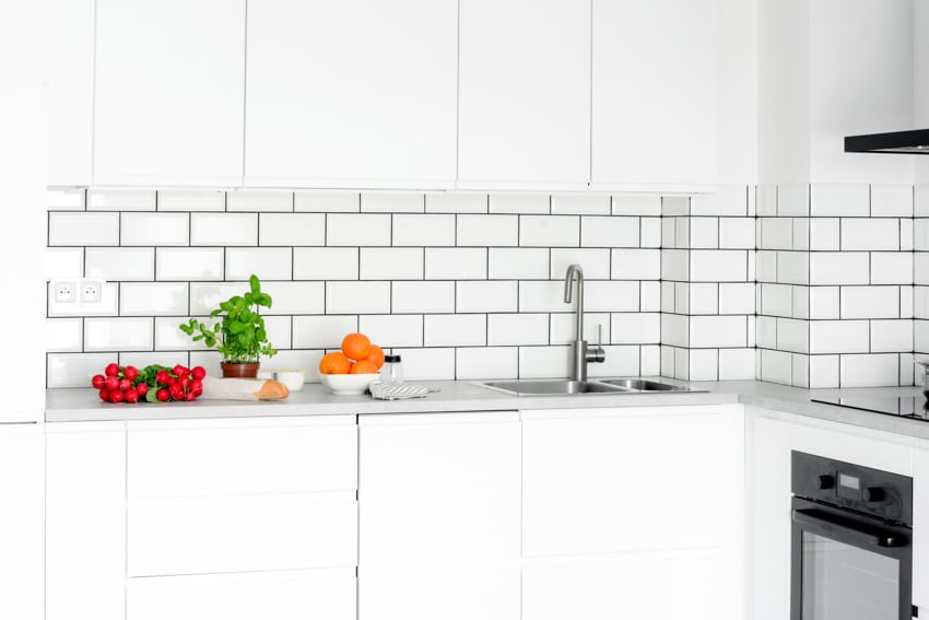 Contemporary kitchen with white subway tile and black grout backsplash, countertop, sink, and oven