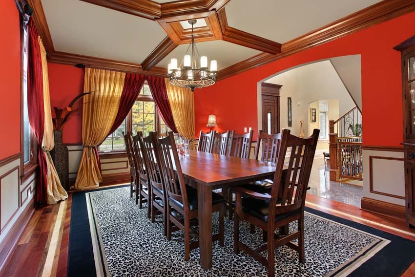 Dining room with Frank Lloyd Wright style dining table, chairs, chandelier, window, red walls, floor carpet, and curtains