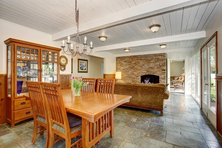 Dining room with mission style chairs, glass cabinet, beadboard ceiling, couch, fireplace, and stone tile floors