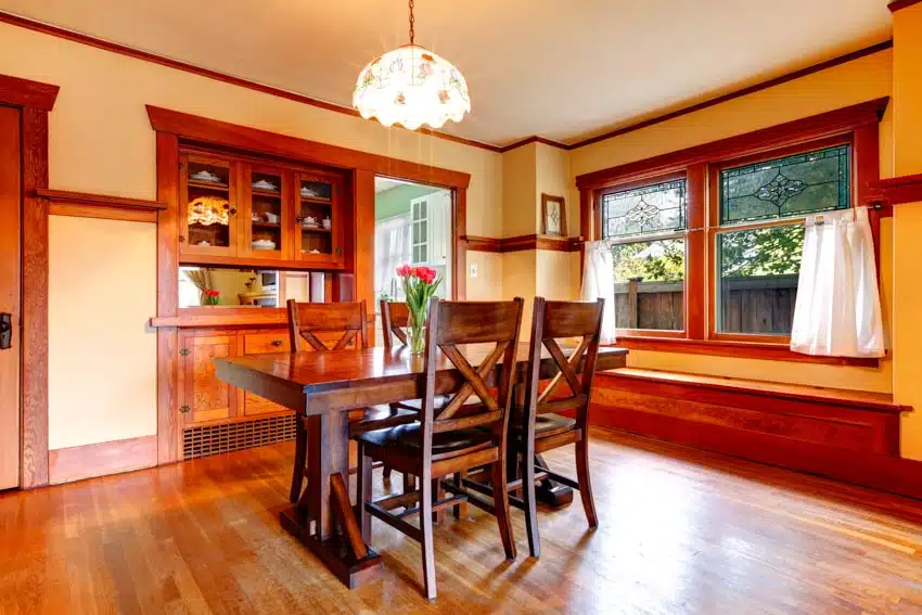 Dining room with primitive wall paint colors, wooden floors, table, chairs, glass cabinet, pendant light, and windows