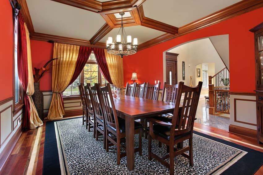 Room with red walls, chairs, wood table, floor carpet, chandelier and curtains