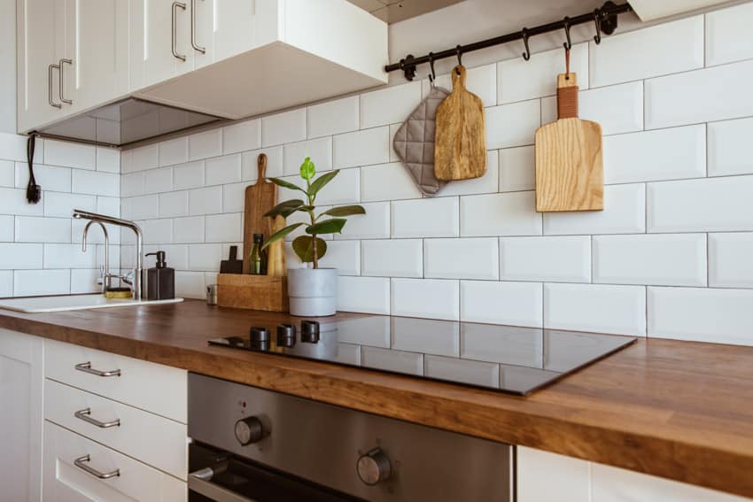 Farmhouse kitchen with matte backsplash tile, wood countertop, stove, and white cabinets
