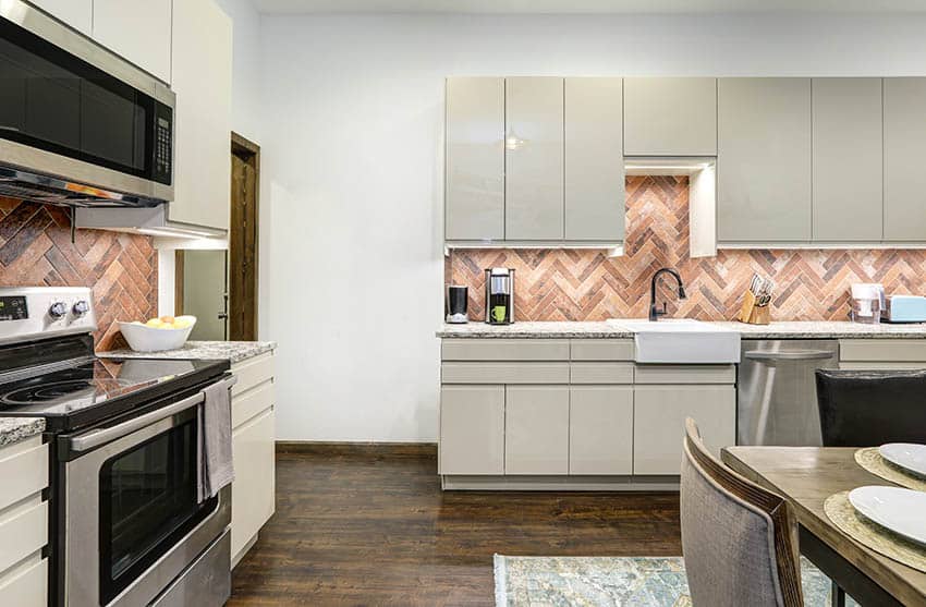 Glossy kitchen cabinets with small cabinet above sink and herringbone pattern backsplash