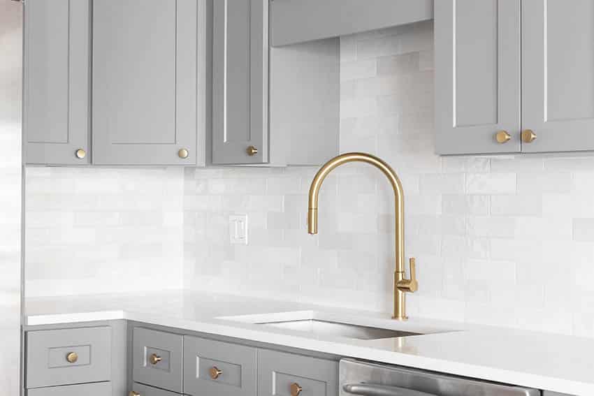 Kitchen with grey cabinets, gold sink faucet, and higher cabinet with white subway tile backsplash