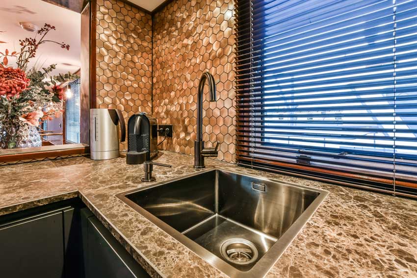 Kitchen with mosaic copper backsplash, granite countertop, stainless steel sink, faucet, and window
