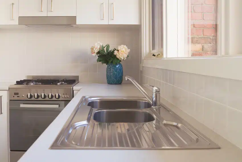 Kitchen with square ceramic tile backsplash, sink, oven, stove, and cabinets