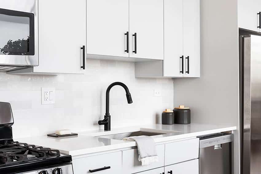 Kitchen with staggered cabinets over sink black hardware white tile