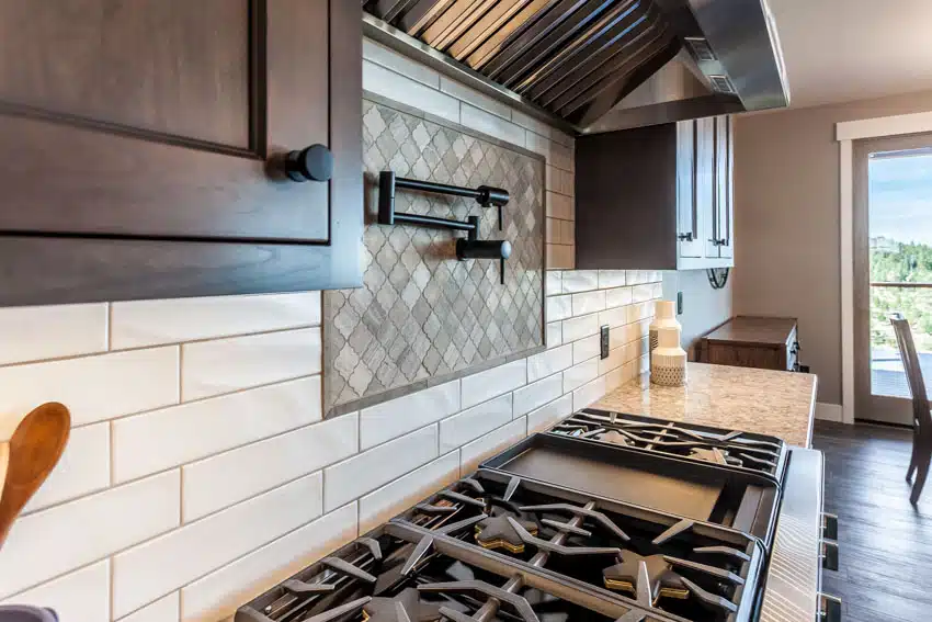 Kitchen with white subway matte backsplash tile, cabinets, stove, and range hood
