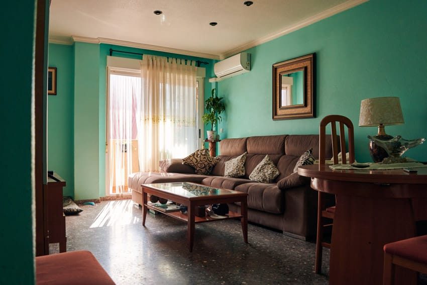 Living room with green primitive wall paint colors, couch, coffee table, lamp, window, and curtain