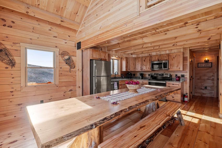 Log cabin dining room with pine wood table, bench, window, and wood wall cladding