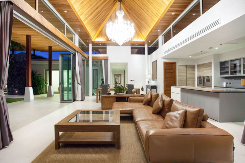 Luxury living room with custom cove ceiling lighting, chandelier, brown leather sofa, coffee table, and floor rug