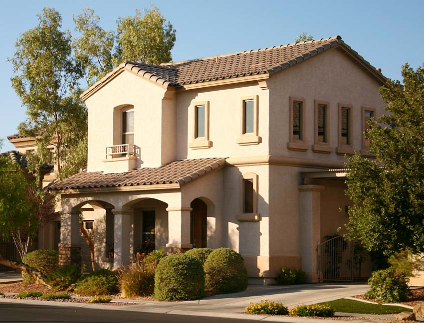 Mediterranean suburban house with stucco wall, shingle roof, windows, hedge plants, and driveway