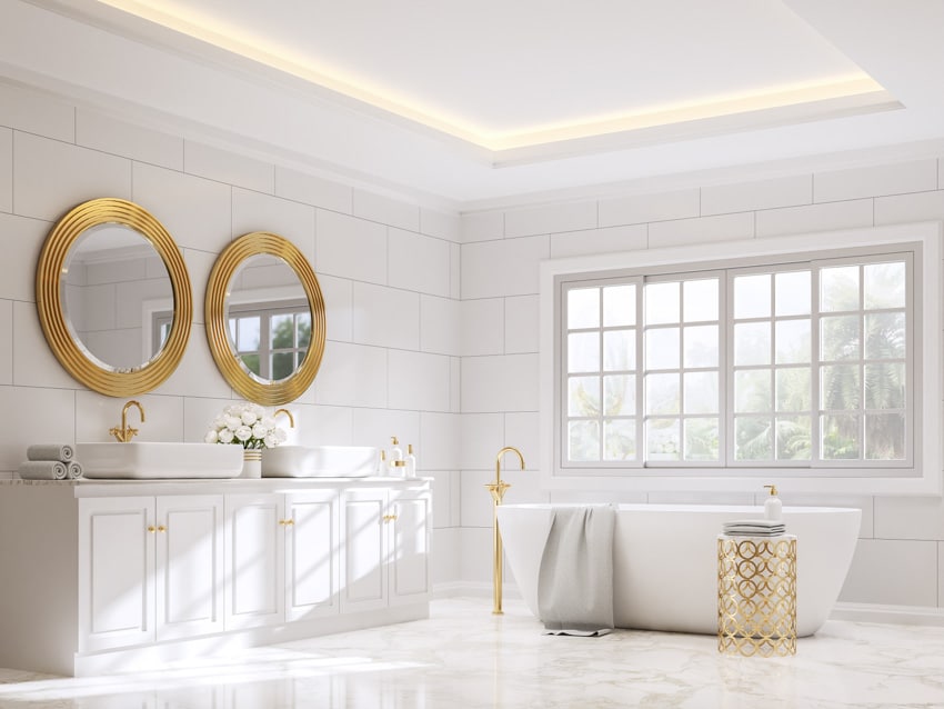 Minimalist bathroom with white tile wall, vanity area, mirrors, cove ceiling lighting, windows, tub, and cabinets