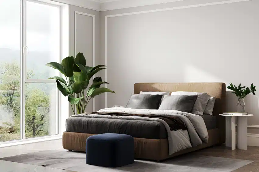 Minimalist bedroom with square pouf, headboard, pillows, bedding, nightstand, indoor plants, and windows