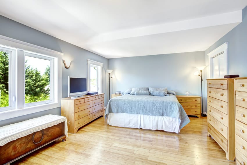 Minimalist bedroom with two dressers, wood floors, windows, television, lamps, and wall sconces