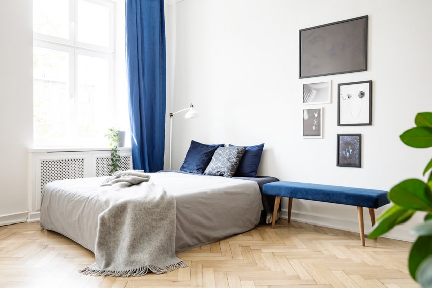 Minimalist bedroom with white walls, cool blue colored curtains, bed, bench, and wood floors