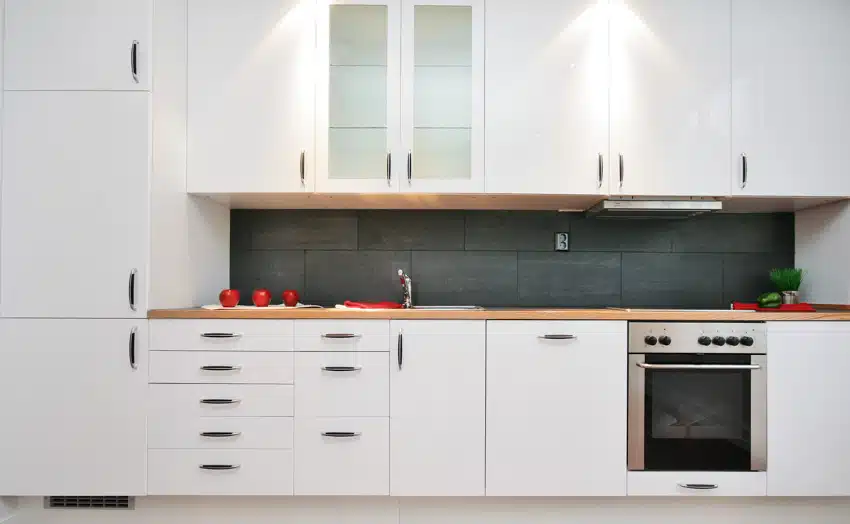 Minimalist kitchen with matte backsplash tile, white cabinets, sink, faucet, and oven
