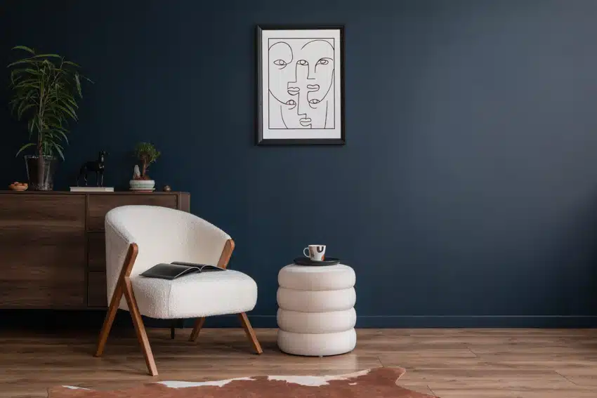 Minimalist living room with accent chair, coffee table pouf, dresser, dark blue wall, and wood flooring