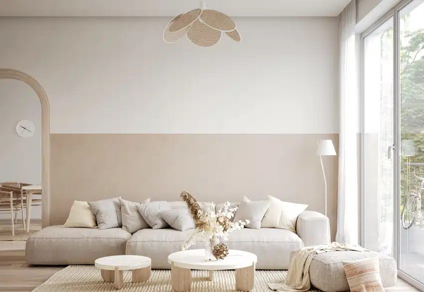 Minimalist living room with sofa, white and beige wall paint colors, coffee table, ottoman, floor lamp, and window