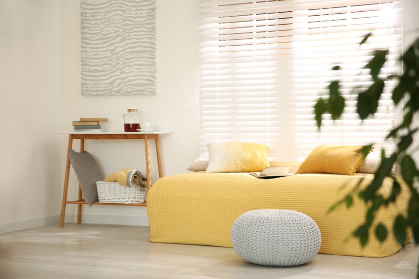 Minimalist living room with yellow couch, pouf, console table, and window shades