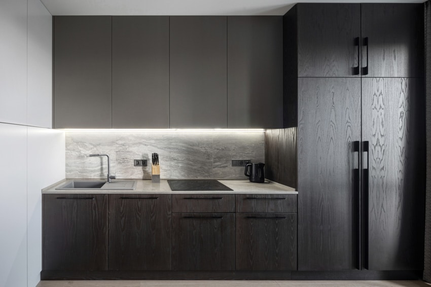 Black kitchen with handleless overhead cabinets, granite backsplash and countertop