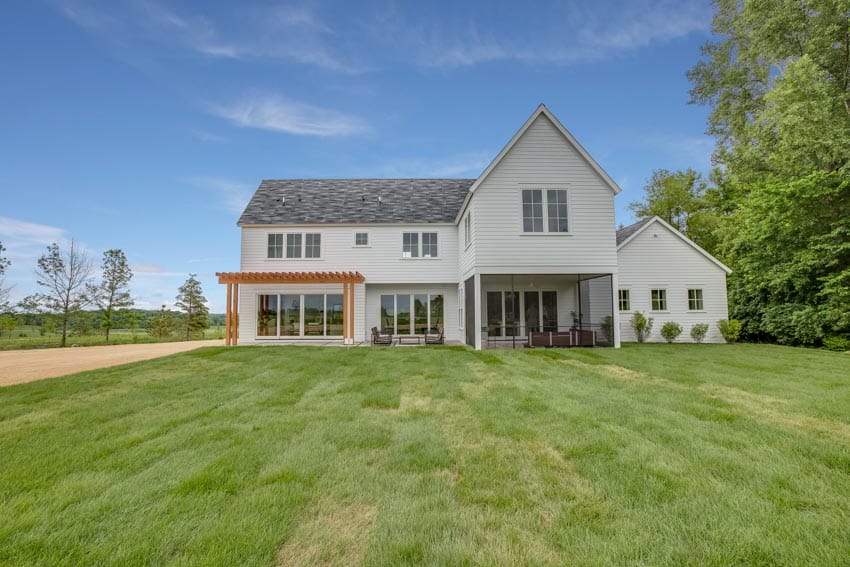 Modern farmhouse with coastal exterior paint colors, outdoor patio, windows, siding, pitched roof, and landscaped lawn
