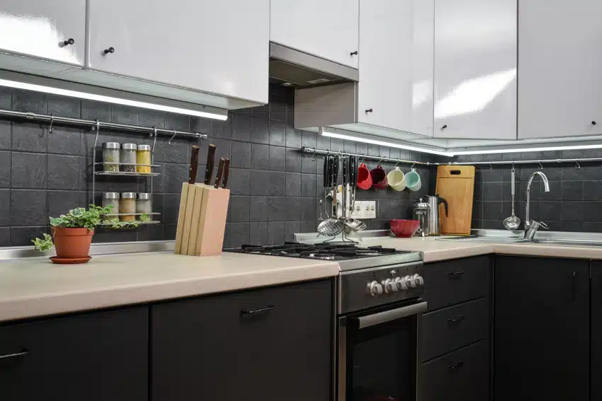 Modern kitchen with black square tile backsplash, countertops, cabinets, stove, and range hood