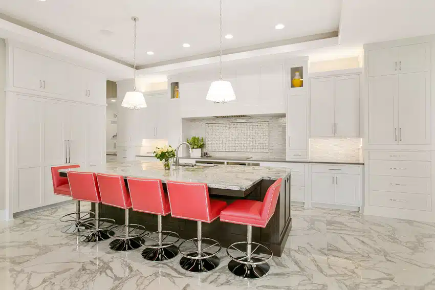 Modern kitchen with polished super white granite countertop, red chairs, pendant lights, white cabinets, and backsplash