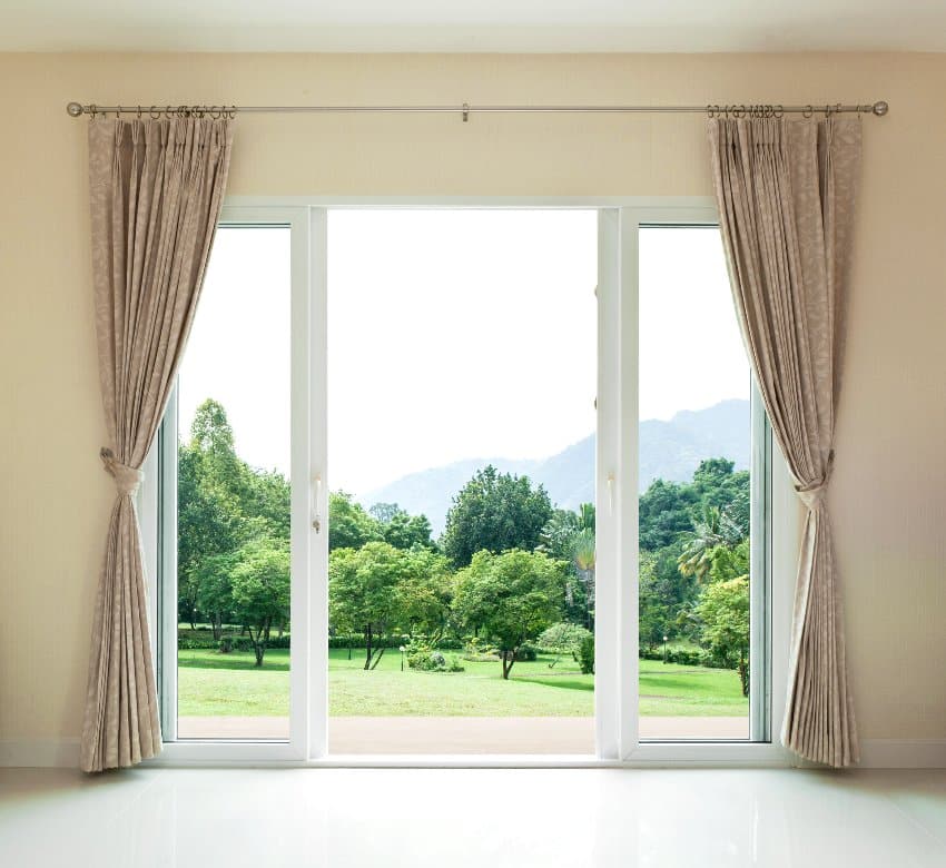 Open glass doors with portiere curtains on the side and an amazing view of green grass and trees