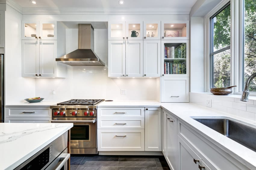 Remodeled contemporary kitchen with white cabinets, countertop, backsplash, oven, stove, range hood, and windows