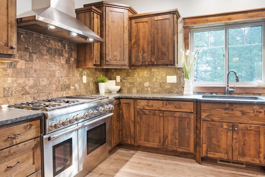 Rustic kitchen with cypress cabinets, textured square tole backsplash, countertop, sink, faucet, range hood, and window