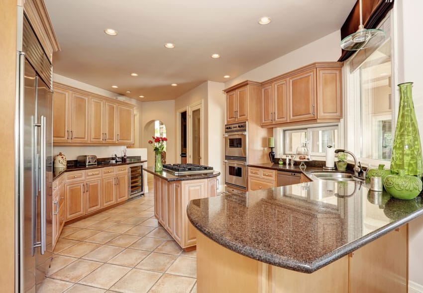 Rustic kitchen with travertine tile floor, countertops, wood cabinets, ceiling lights, and island