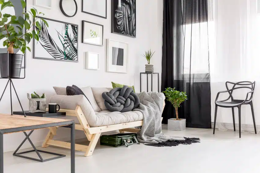 Scandinavian living room with white walls, futon couch, indoor plants, side table, and accent chair