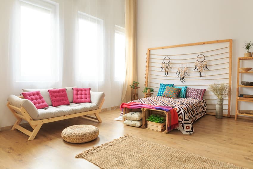 Scandinavian bedroom with futon couch, round pouf, bedding, custom headboard, freestanding shelves, windows, and curtains