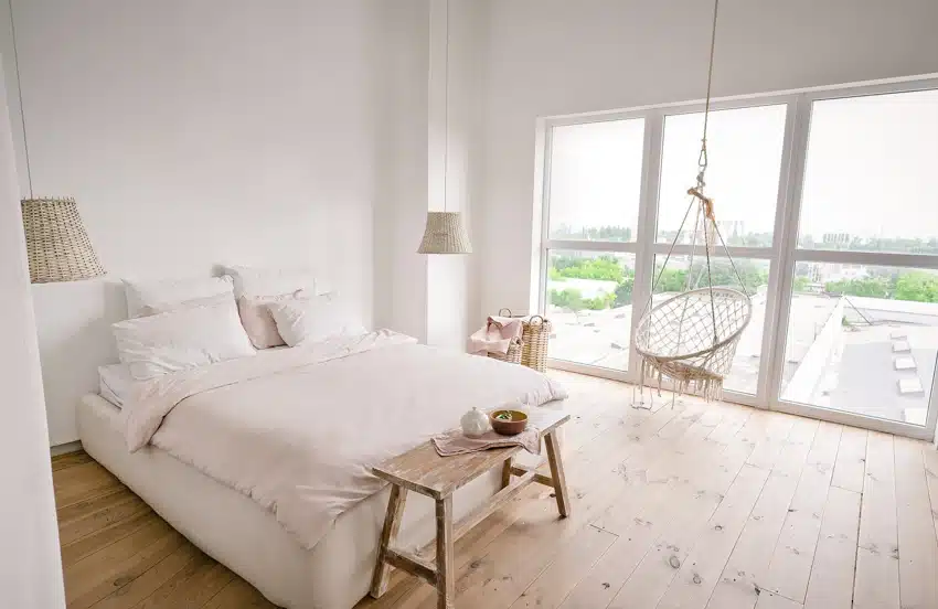 Scandinavian bedroom with swinging chair, bedding, pillows, hanging lamps, wood flooring, and windows