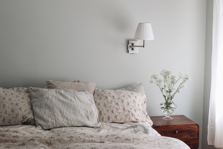 Simple bedroom with wall sconce, pillows, vase, and nightstand