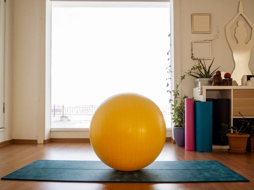Simple living room with yoga ball as bean bag alternative, floor mat, wooden flooring, dresser, and window