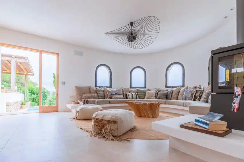 Spacious and bright living room with ottoman pouf, curved sofa, pillows, rug, ceiling fan, and glass door
