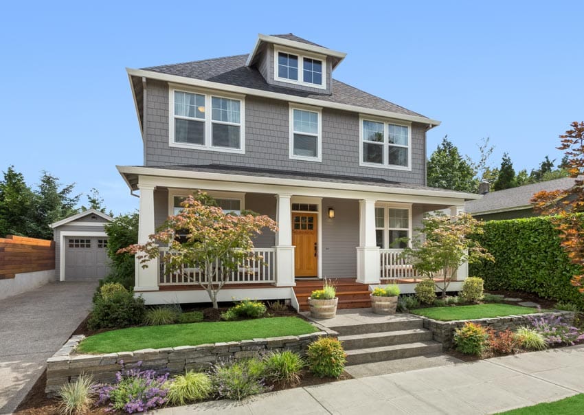 Suburban house with hedge plants, dormer, windows, front door, porch, and wall cladding