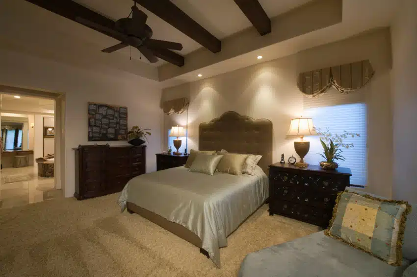 Traditional bedroom with two dressers, comforter, pillows, headboard, ceiling fan, carpet floors, and lighting fixtures